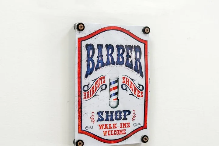 Insegna vintage Barber Shop, Haircuts and Shaves, Walk-ins welcome, appesa al muro bianco